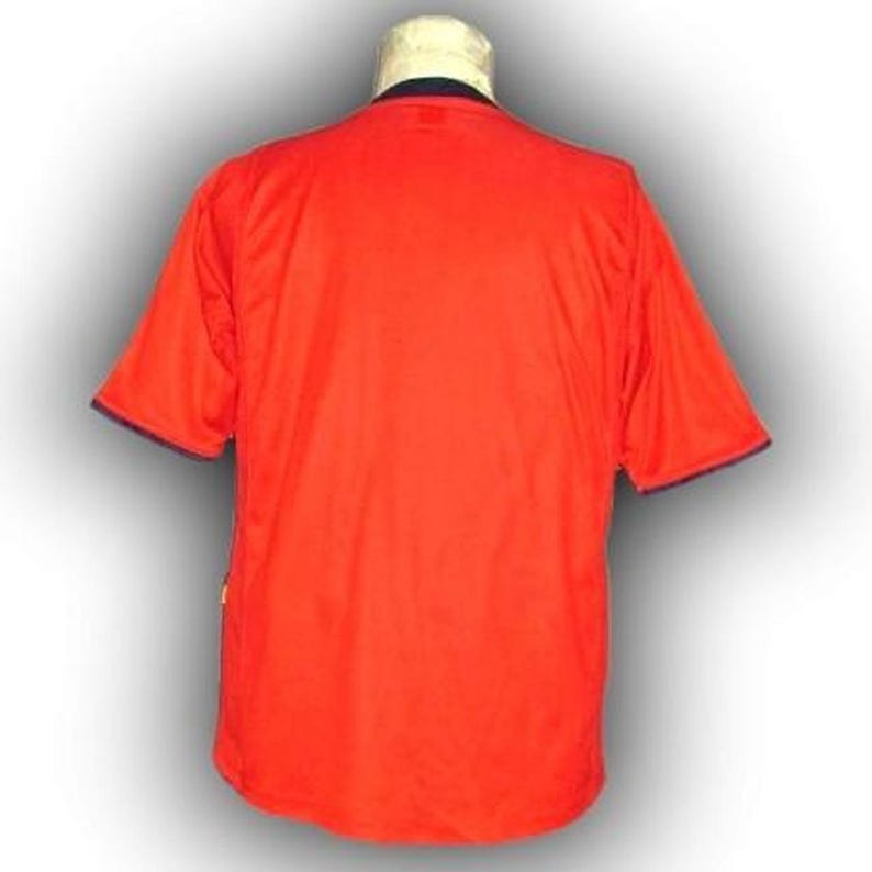 Op de afbeelding: Een fel oranje shirt met korte mouwen en marineblauwe afwerking op de kraag en mouwen. Het shirt wordt op een mannequin getoond. De achterkant van het shirt is zichtbaar en toont het eenvoudige ontwerp en de effen kleur.