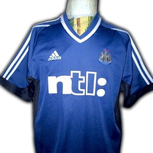 May include: A blue Adidas soccer jersey with white stripes on the sleeves and a white V-neck collar. The jersey features the text "ntl:" in white block letters and a team crest.