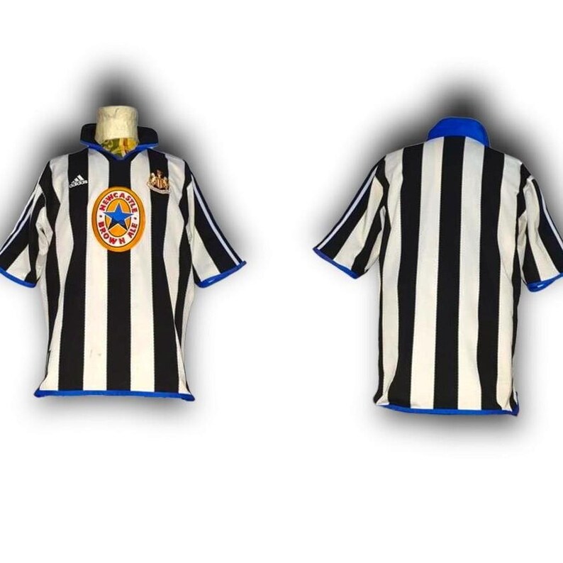 Op de afbeelding: Twee Newcastle United voetbalshirts. E&eacute;n shirt wordt van voren bekeken en de andere van achteren. De shirts zijn zwart-wit gestreept met blauwe accenten. Het shirt aan de voorkant heeft een teamlogo.