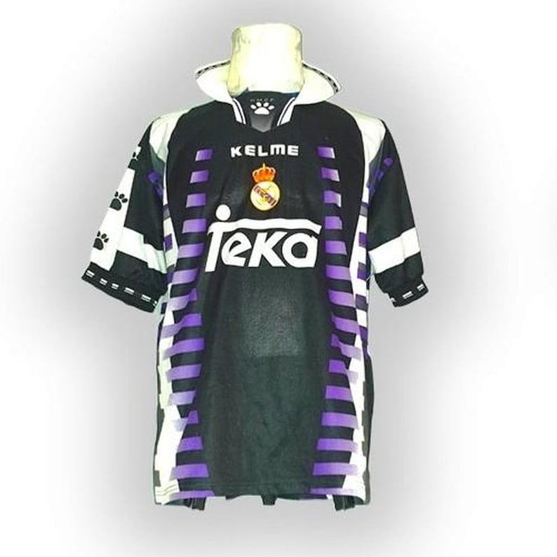 May include: Black and purple soccer jersey with white accents. The jersey features the "Kelme" logo, a crown emblem, and the "Teka" sponsor logo. The sleeves have paw print designs.
