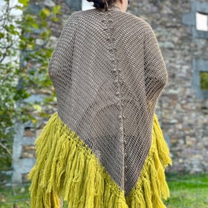 May include: A triangular crochet shawl featuring a taupe open-knit mesh pattern with a central vertical row of small decorative bobbles and a long, thick fringe in a vibrant chartreuse yellow along the bottom edges.
