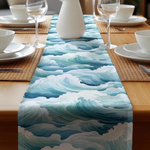 May include: A white table runner with a blue and white wave pattern. The runner is laid out on a wooden table with place settings.