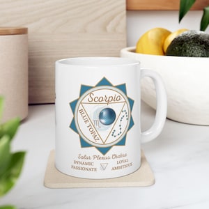 May include: White ceramic mug featuring a blue and gold Scorpio design with the words "Scorpio" and "Blue Topaz". The mug also includes text about the Solar Plexus Chakra, with words like "Dynamic" and "Passionate".