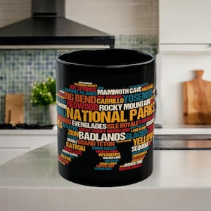 Könnte beinhalten: Schwarze Keramiktasse mit einer bunten Wortwolke, die die Namen verschiedener Nationalparks in den Vereinigten Staaten zeigt. Das Wort "NATIONAL PARKS" ist in großen, gelben Buchstaben geschrieben.