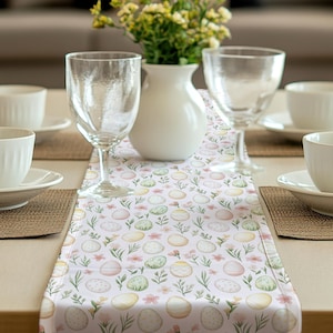 Peut inclure: Un chemin de table blanc avec un fond rose pastel et un motif répété de feuilles vertes, de fleurs roses et d'œufs de Pâques colorés.