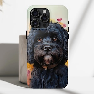 May include: A black and white phone case featuring a cute black dog illustration. The dog has a fluffy coat and is looking at the camera. The background is a soft yellow with pink flowers.