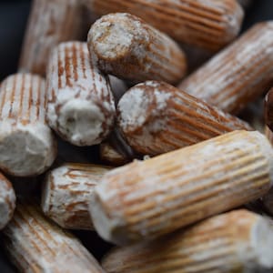 May include: Close-up of a pile of wooden dowels. The dowels are cylindrical with a light brown color and visible wood grain. The ends are white. The dowels are used for woodworking and construction.