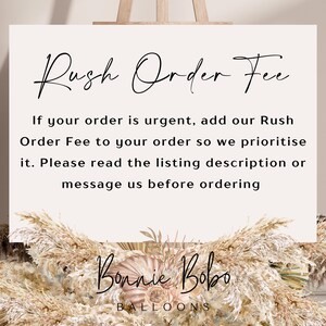 May include: White sign with black text that reads "Rush Order Fee". The text below explains that if your order is urgent, you can add a rush order fee to your order. The sign also says to read the listing description or message the seller before ordering. The sign is decorated with dried pampas grass and the text "Bonnie Bobo Balloons" is at the bottom.