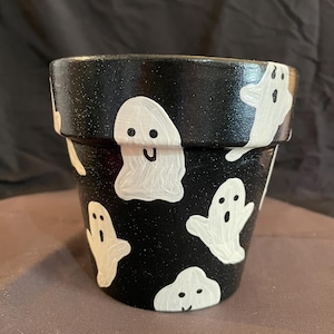 May include: Black terracotta planter with white ghost illustrations. The ghosts have simple eyes and mouths.