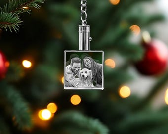 May include: A silver keychain with a square crystal charm featuring a black and white photo of a couple and their dog. The charm is hanging from a silver chain.