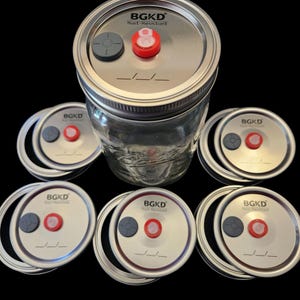 May include: A collection of clear glass jars with metal lids. Each lid has a gray and red component, with the text "BGKD Rust-Resistant" printed on the lid. The jars are arranged against a black background.