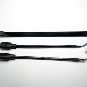 Può includere: Tre cavi USB-C neri di diverse lunghezze sono mostrati su uno sfondo bianco. Il cavo superiore è piatto e largo, mentre gli altri due sono rotondi. I due cavi inferiori hanno connettori con fili colorati.