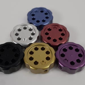 Puede incluir: Seis pomos redondos con un patrón circular de agujeros. Los pomos son de diferentes colores: plateado, negro, dorado, morado, rojo y azul.