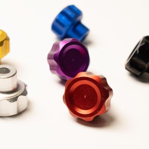 May include: A collection of colorful, fluted knobs in gold, silver, blue, purple, red, and black. These small, decorative knobs have a circular top and a cylindrical base, suitable for various applications.
