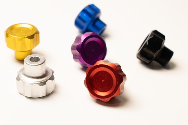 Puede incluir: Una colecci&oacute;n de perillas acanaladas de colores: dorado, plateado, azul, morado, rojo y negro. Estas peque&ntilde;as perillas decorativas tienen una parte superior circular y una base cil&iacute;ndrica, adecuadas para diversas aplicaciones.