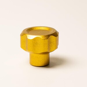 Puede incluir: Tirador de armario dorado con una parte superior circular y estriada y una base cil&iacute;ndrica. El tirador tiene un dise&ntilde;o sencillo, adecuado para varios estilos de muebles. El acabado met&aacute;lico a&ntilde;ade un toque de sofisticaci&oacute;n. El tirador es probablemente de metal.