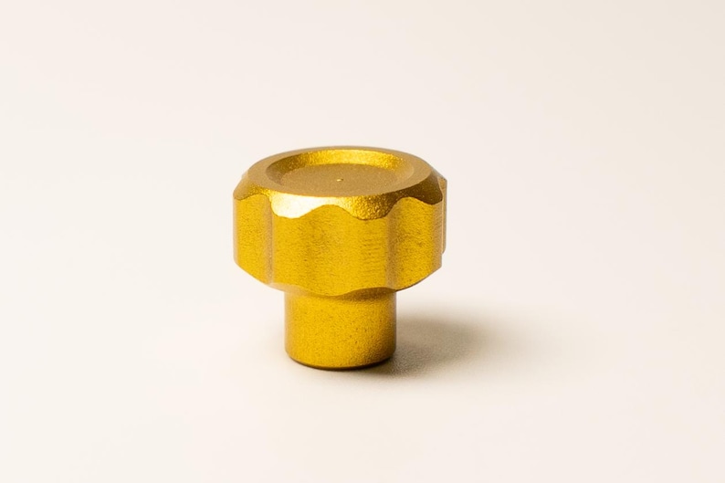 Puede incluir: Tirador de armario dorado con una parte superior circular y estriada y una base cil&iacute;ndrica. El tirador tiene un dise&ntilde;o sencillo, adecuado para varios estilos de muebles. El acabado met&aacute;lico a&ntilde;ade un toque de sofisticaci&oacute;n. El tirador es probablemente de metal.