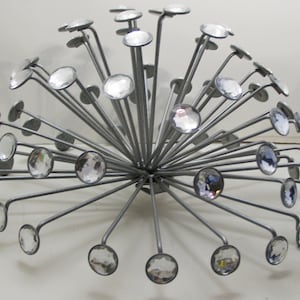 May include: A spherical decorative object featuring numerous thin, silver-toned metal rods radiating from a central point. Each rod terminates in a circular, faceted clear crystal accent, creating a starburst or dandelion-like structure.