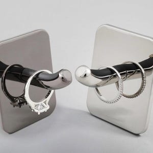 May include: Two silver ring holders with a black rubber ring holder attached to the top. One holder is black and the other is silver. Both holders have rings on them.