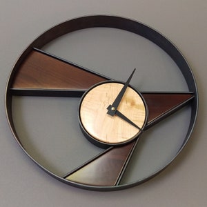 May include: A modern wall clock with a black metal frame and wooden accents. The clock face is divided into sections with a wood veneer finish. The clock hands are black.