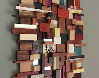 Puede incluir: Una pieza de arte de pared hecha de varios bloques de madera en diferentes colores y texturas. Los bloques están dispuestos en un patrón aleatorio, creando un diseño moderno y abstracto.