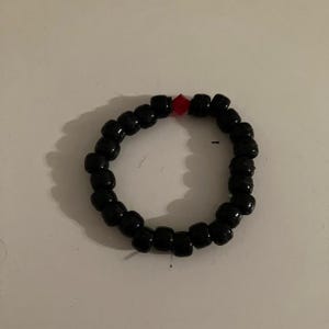 Puede incluir: Un brazalete de cuentas negras con una sola cuenta roja.