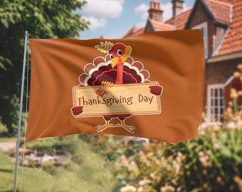 May include: A brown Thanksgiving Day flag waving in the wind. The flag features a cartoon turkey holding a sign that reads "Thanksgiving Day". The background includes a house and green foliage.