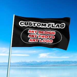 May include: A black custom flag waving in the wind against a blue sky. The flag has white text that reads "CUSTOM FLAG" and a white-bordered oval with the words "ANY DESIGN, ANY PHOTO, ANY LOGO" in red.