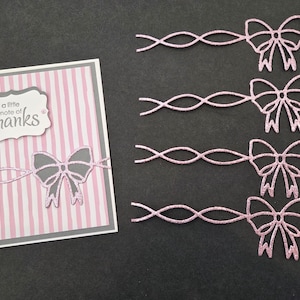 May include: A greeting card with a pink and white striped background and a gray border. The card features a gray bow and the text "a little note of thanks". Four pink glitter bows are also present.