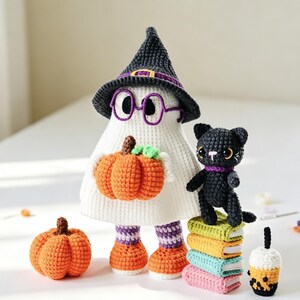 May include: A white crocheted ghost figure wearing a black witch hat and purple glasses, holding an orange pumpkin. Beside it stands a small black crocheted cat on a stack of four colourful books, with an extra pumpkin and a boba tea drink nearby.