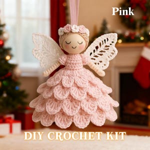 May include: A pink crochet angel decoration with white lace wings and a floral crown. The angel has a wooden head with closed eyes and a smiling face. The text "Pink" and "DIY CROCHET KIT" are displayed.