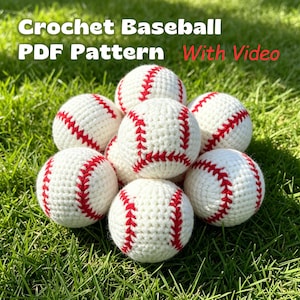 May include: A collection of eight handmade crochet baseballs, each featuring a white yarn base with red stitched seams. The text "Crochet Baseball PDF Pattern With Video" is overlaid in white and red lettering across the top of the image.