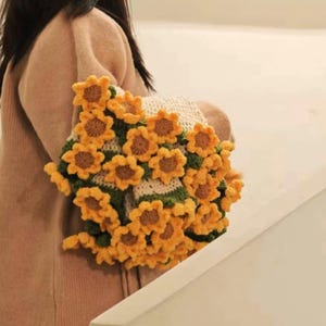 K&ouml;nnte beinhalten: Ein geh&auml;keltes Schals in Sonnenblumenform mit gelben und gr&uuml;nen Blumen. Der Schal ist aus Garn gefertigt und ein einzigartiges und stilvolles Accessoire.