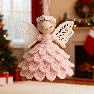 May include: A handcrafted Christmas angel ornament. The angel has a wooden head, crocheted pink dress, and white lace wings. A pink ribbon is attached for hanging. The angel is decorated with a floral crown and has closed eyes.