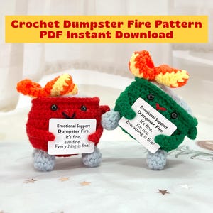 May include: Two handmade crochet dumpster figures, one red and one green, each holding a sign that reads "Emotional Support Dumpster Fire." The figures have orange and yellow flames and gray feet. The text "Crochet Dumpster Fire Pattern PDF Instant Download" is at the top.