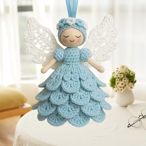 May include: A handmade crochet angel doll with a light blue dress and white wings. The doll has a smiling face, a blue bonnet with white flowers, and a blue ribbon for hanging. The angel is a decorative item.
