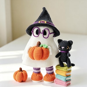 May include: A white crocheted ghost figure wearing a black witch hat with a purple band and purple glasses, holding an orange pumpkin. Beside it stands a small black crocheted cat next to a stack of four colourful books and a separate orange pumpkin.