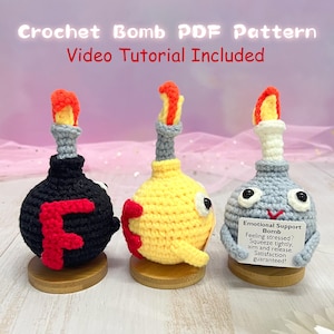 Peut inclure: Trois bombes au crochet faites à la main avec des visages de dessins animés et des flammes. L'une est noire avec un "F" rouge, l'autre est jaune avec un accent rouge, et la dernière est grise avec un panneau indiquant "Emotional Support Bomb". Le texte "Crochet Bomb PDF Pattern Video Tutorial Included" est en haut.