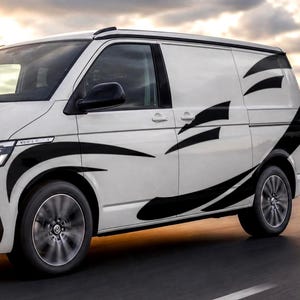 May include: A white van featuring black graphic decals along the side panels. The design consists of sharp, sweeping lines and angular shapes that extend from the front wheel arch across the doors and toward the rear of the vehicle body.