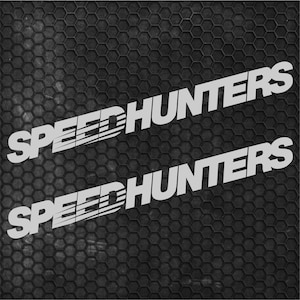 Pode incluir: Dois autocolantes em vinil branco com o texto SPEEDHUNTERS numa fonte a negrito e inclinada. A palavra SPEED tem linhas de movimento horizontais integradas nas letras, enquanto HUNTERS está numa fonte de bloco sólido. Fundo escuro.