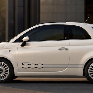 Op de afbeelding: Een witte tweedeurs hatchback auto met een zwarte grafische sticker op het zijpaneel. De sticker toont het getal 500 in een gestileerd lettertype gevolgd door drie horizontale parallelle lijnen. De auto heeft zilverkleurige meerspaaks wielen.