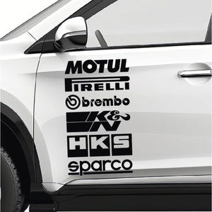 May include: A white car door featuring a vertical stack of black automotive brand decals. The logos displayed from top to bottom are Motul, Pirelli, Brembo, K&N, HKS, and Sparco. The decals are applied to the front passenger side door panel.