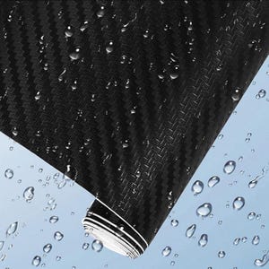 Puede incluir: Rollo de envoltura de vinilo de fibra de carbono negro con un patr&oacute;n de tejido texturizado. El rollo est&aacute; parcialmente desenrollado, revelando las rayas interiores blancas y negras. Gotas de agua est&aacute;n dispersas por la superficie, lo que sugiere una funci&oacute;n impermeable.