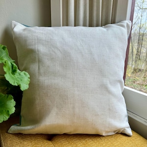 Puede incluir: Una almohada blanca con un borde turquesa. La almohada est&aacute; hecha de una tela suave y texturizada.