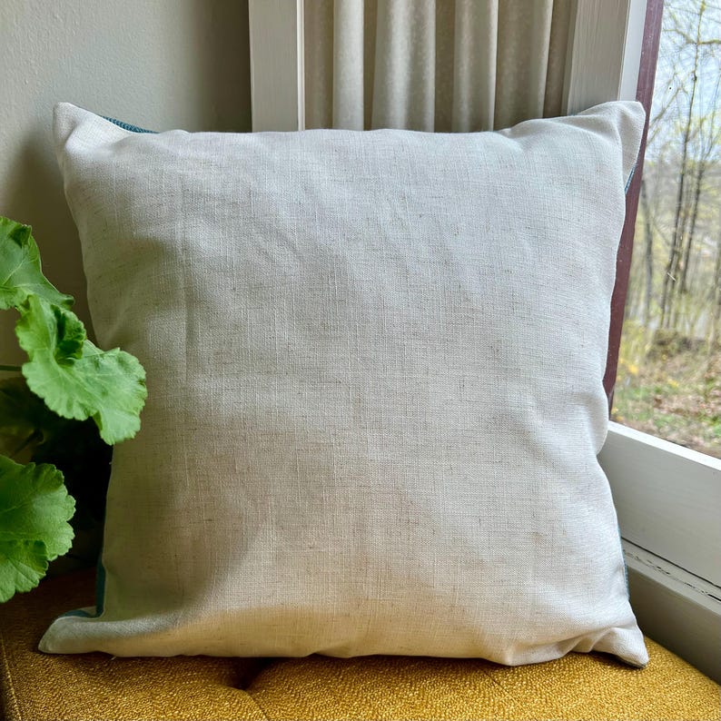 Puede incluir: Una almohada blanca con un borde turquesa. La almohada est&aacute; hecha de una tela suave y texturizada.