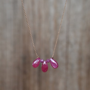 May include: A delicate gold chain necklace with three teardrop-shaped ruby gemstones.