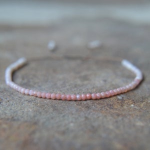 May include: A delicate pink opal beaded bracelet with a simple design. The bracelet is made with small, round beads that are strung together on a thin cord.