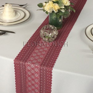 May include: A burgundy lace table runner with a delicate diamond pattern. The runner is 14 inches wide and 72 inches long. It is perfect for adding a touch of elegance to any table setting.