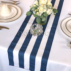 May include: A white tablecloth with a navy blue and white striped table runner. The table runner is 12 inches wide and has 5 stripes. The table runner is decorated with a vase of white flowers and a crystal candle holder.
