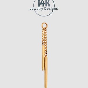 Könnte beinhalten: Ein goldfarbener Anhänger mit Kette und zwei vertikalen Stäben. Das Schmuckstück hängt an einer filigranen Kette und hat eine polierte Oberfläche. Der Text "14k Jewelry Designs" befindet sich in einem Kreis über dem Anhänger.